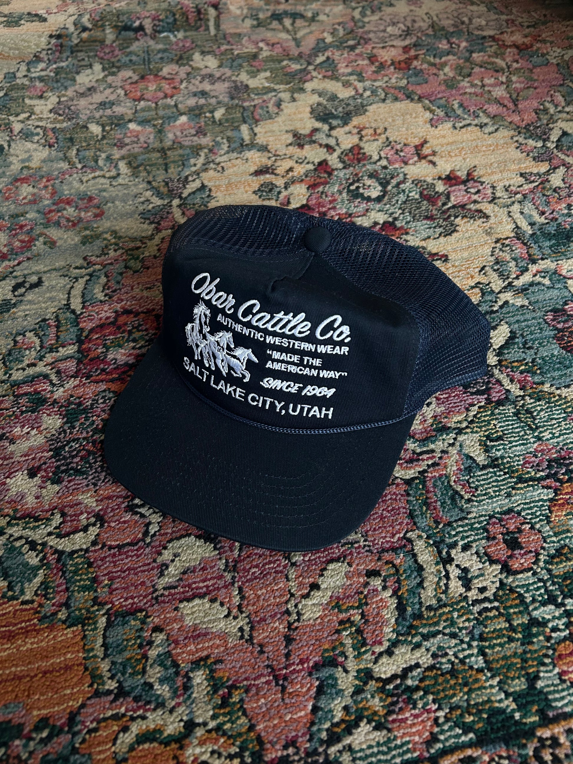 Navy blue cap with white text and logo on a patterned rug