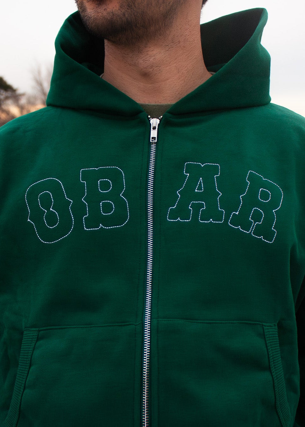 Person wearing a green hoodie with 'OBAR' text in an open outdoor setting